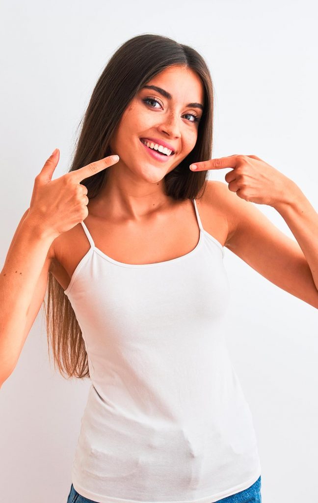 mujer joven sonriendo apuntando con los dedos a su sonrisa