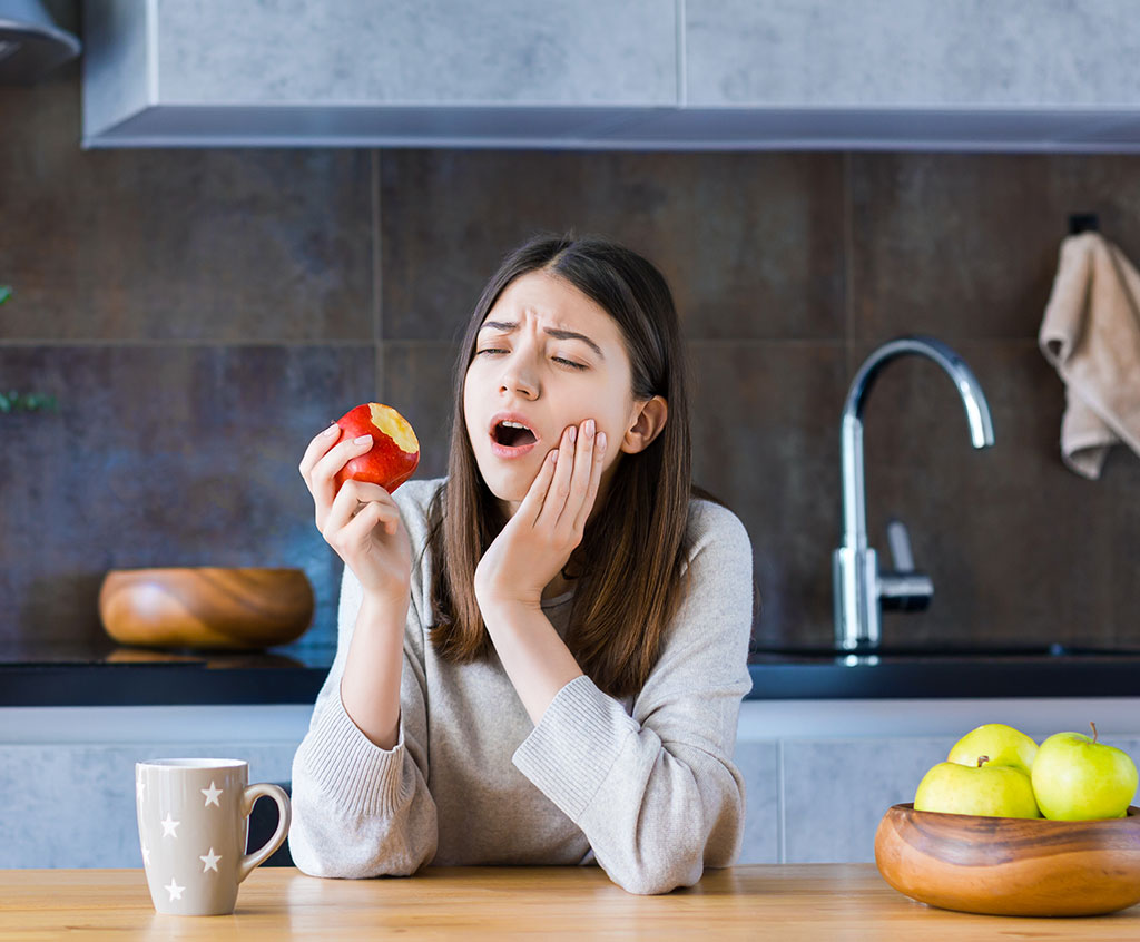 chica experimenta dolor en los dientes al comer una manzana